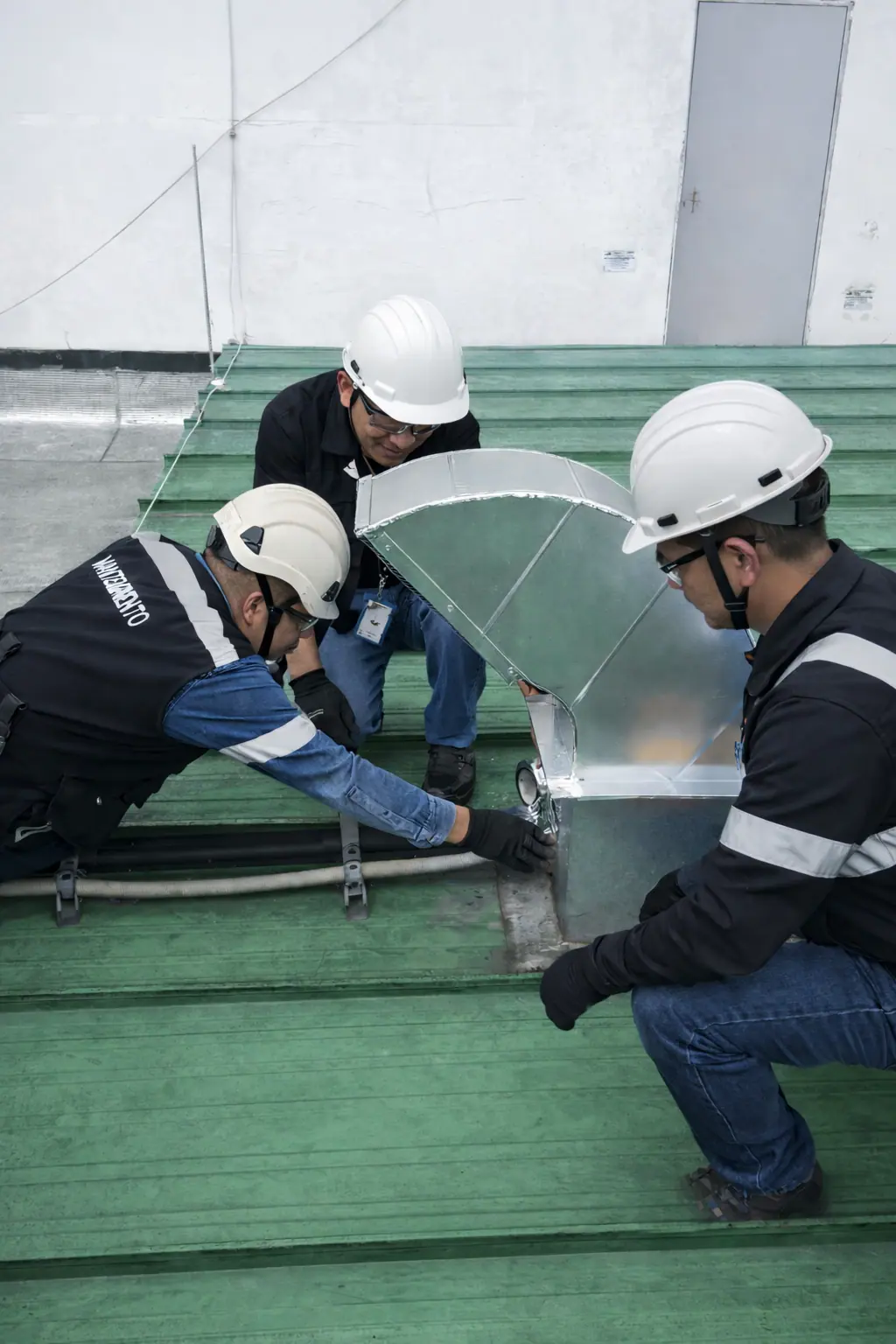 Equipo de tres técnicos montando una transición de ducto galvanizado sobre una cubierta metálica industrial